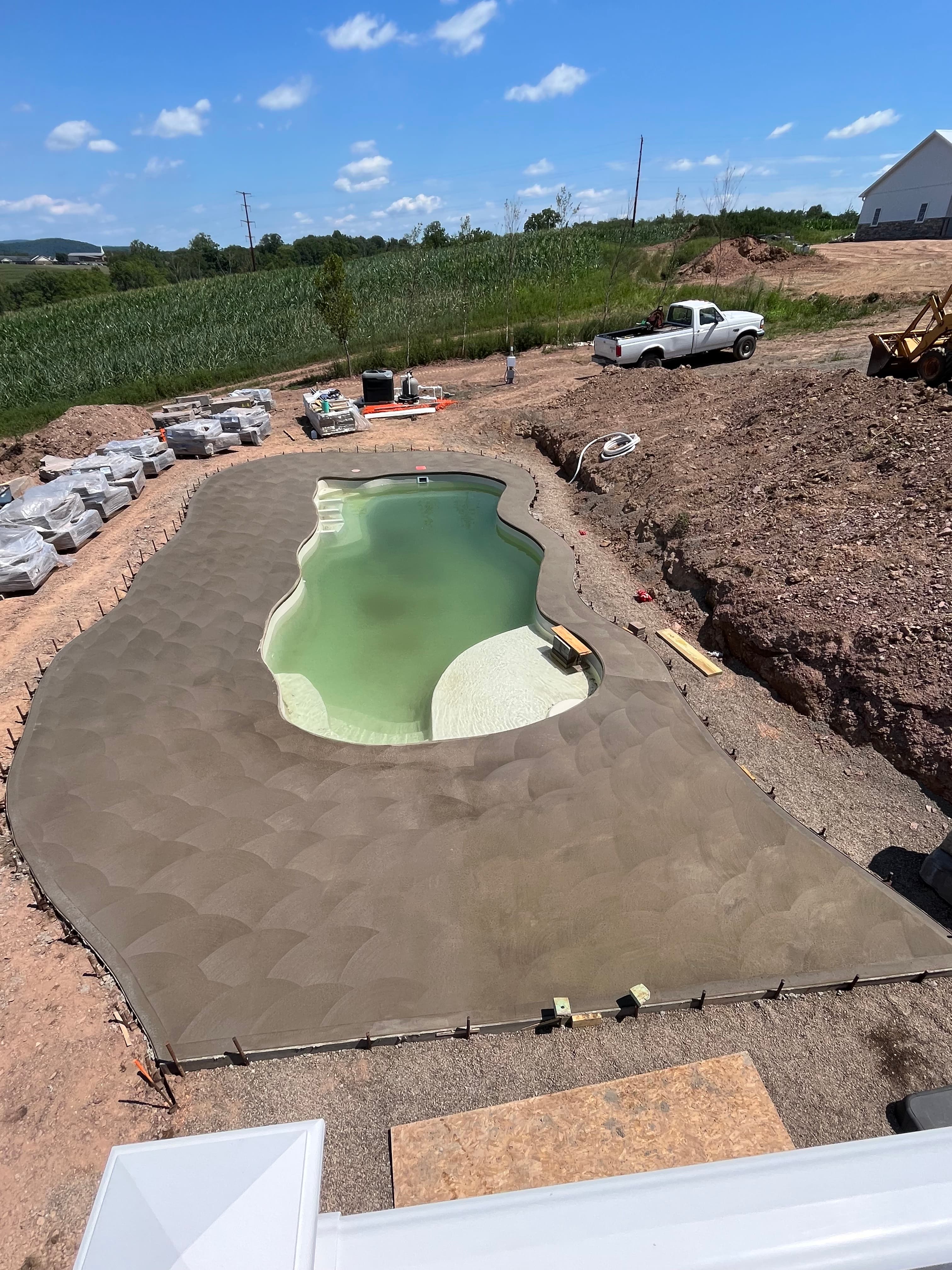 Freeform swimming pool under construction with a large, freshly poured and textured concrete patio.