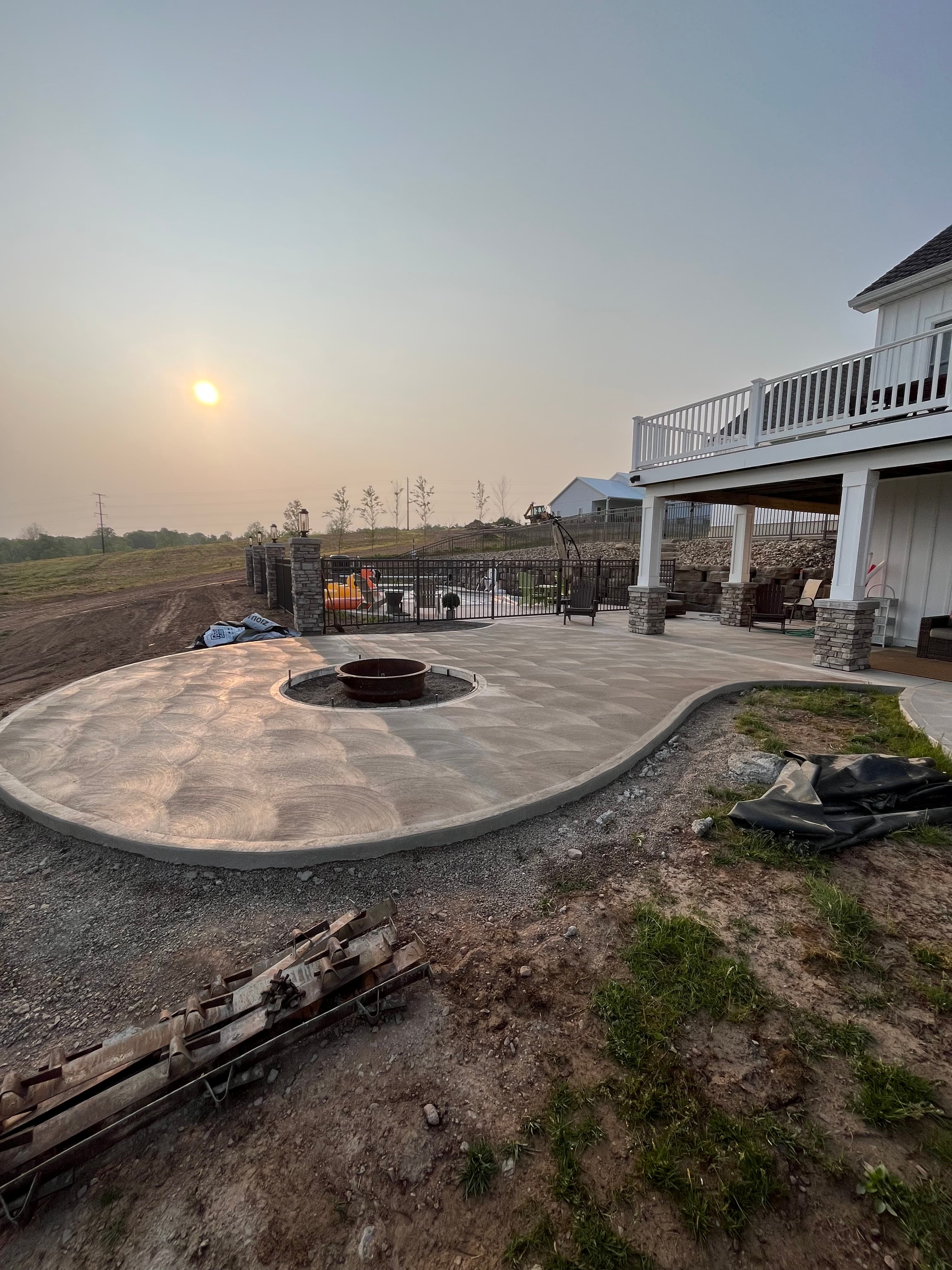 Curved concrete patio with a swirl finish and fire pit under a hazy sunset.