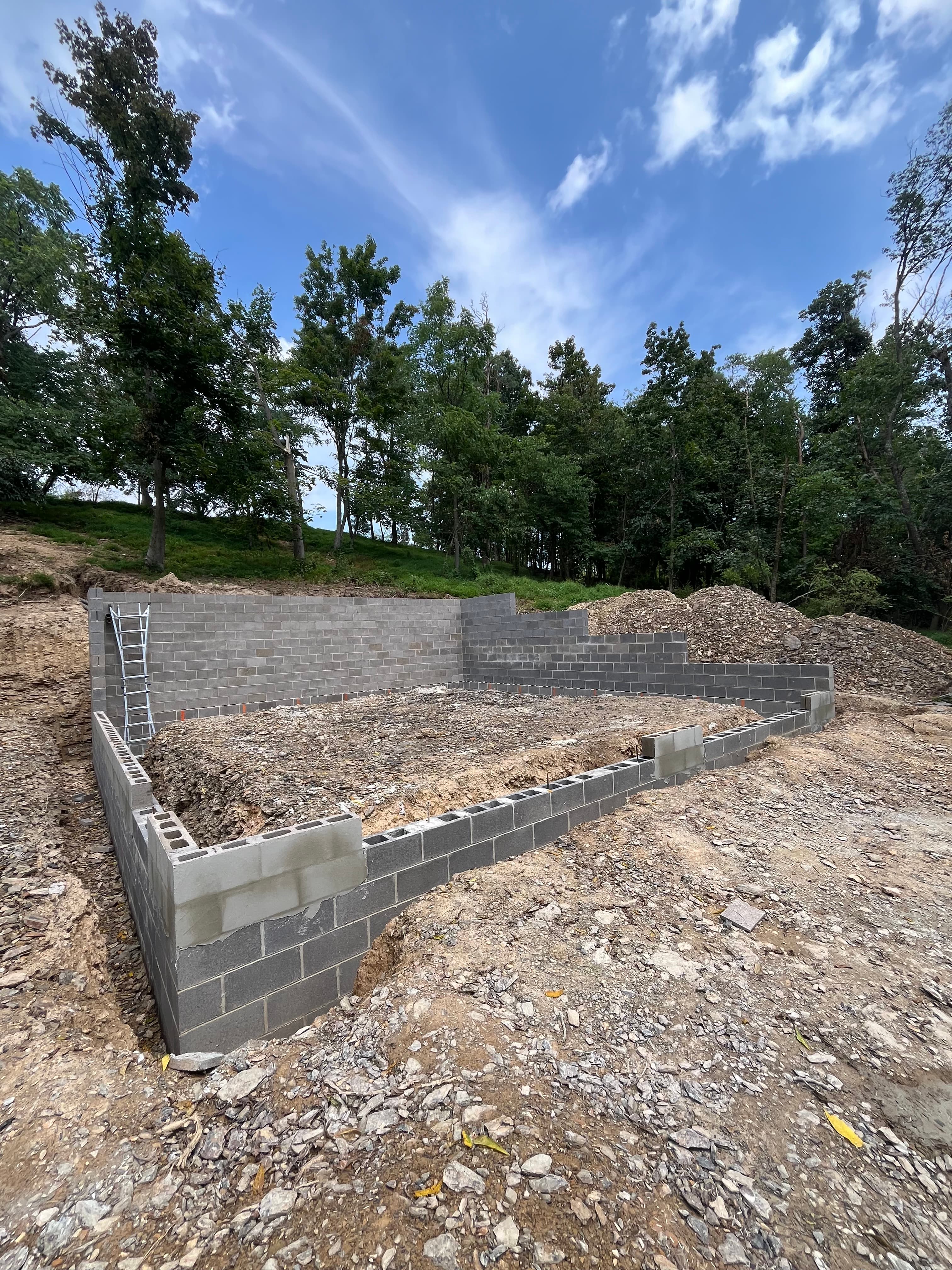 Cinder block foundation walls under construction on a dirt site with a forest background.