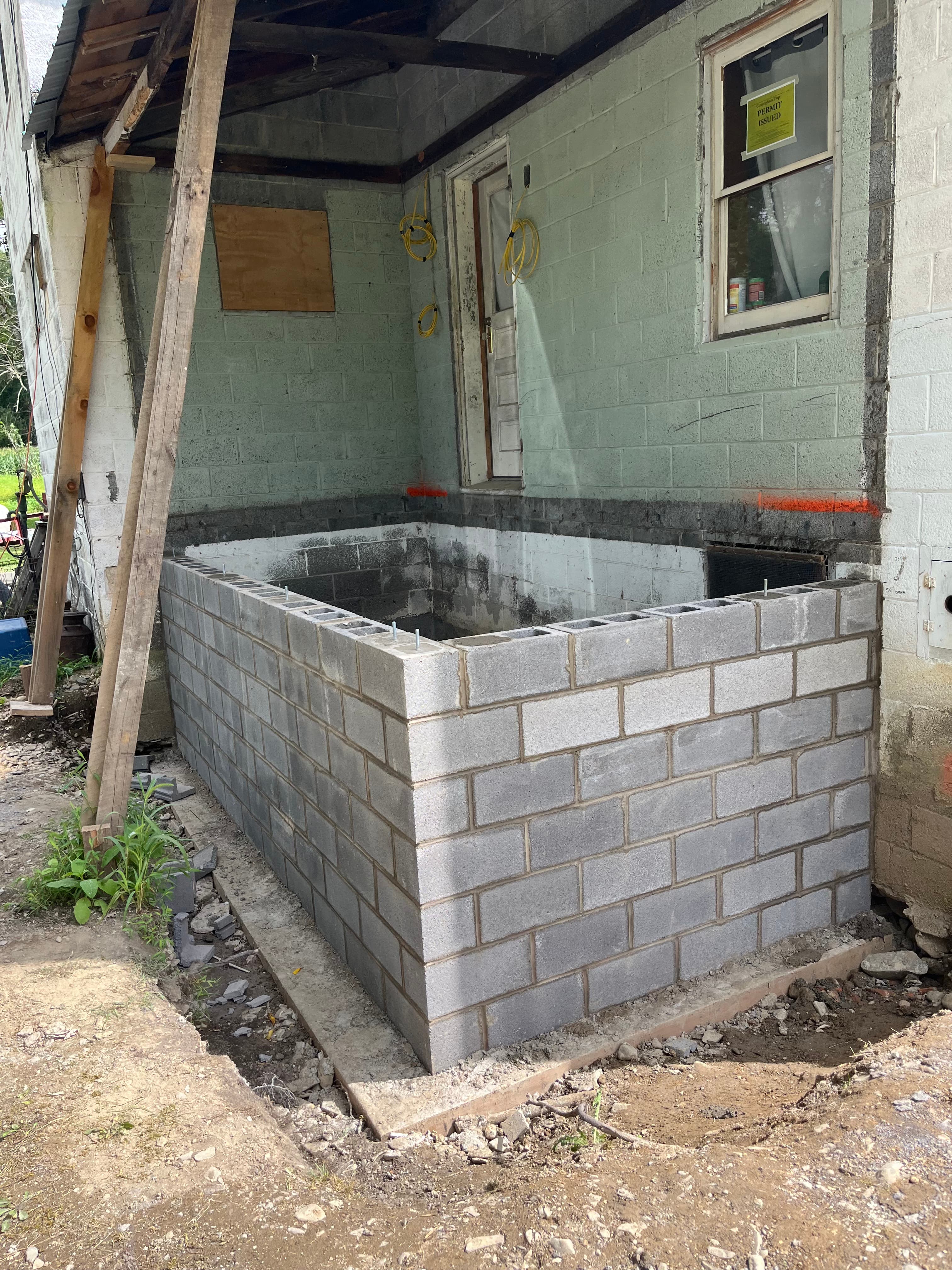 Concrete block wall under construction against a building with a permit sign in the window.