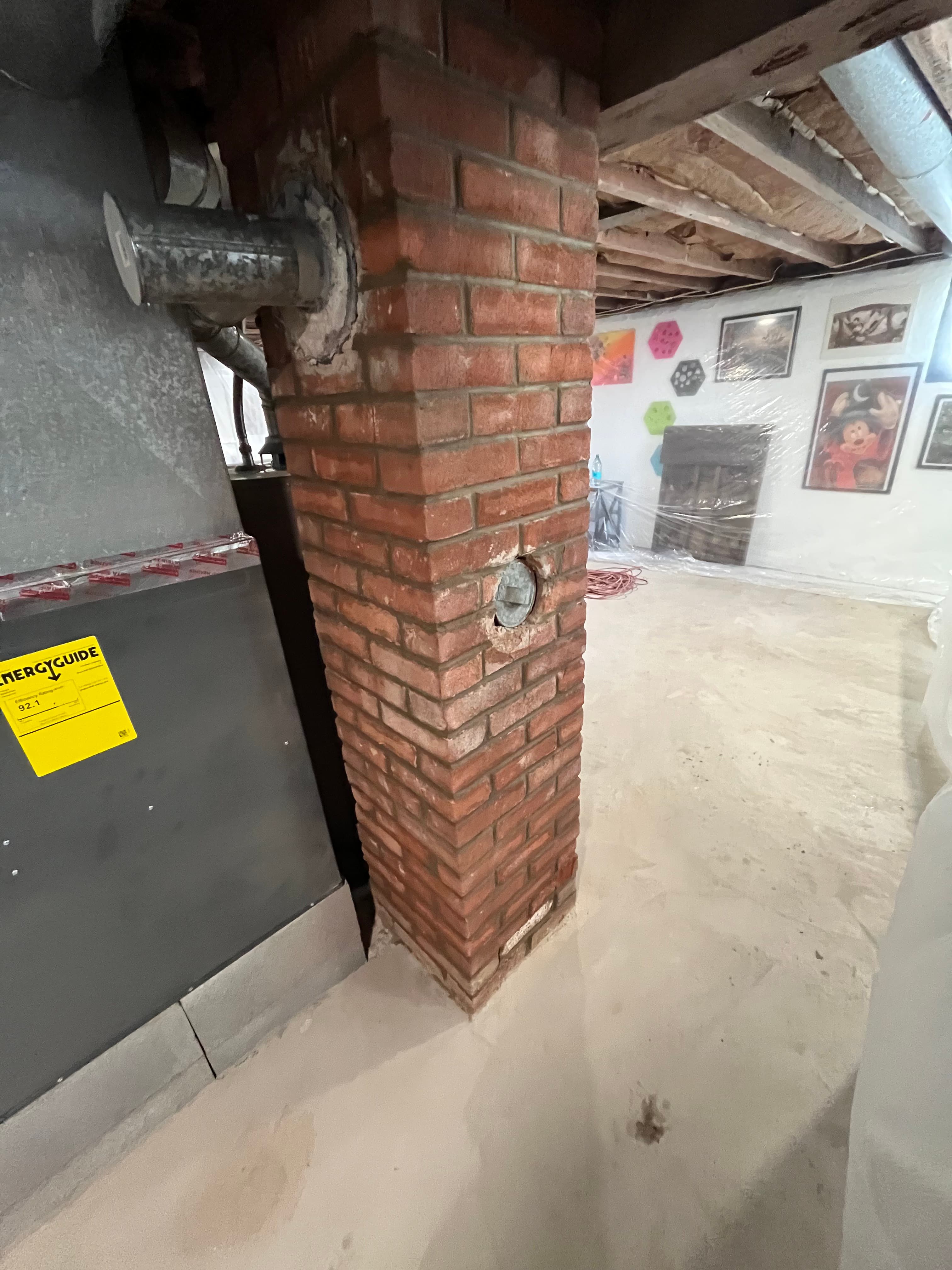 Red brick chimney with a metal flue pipe and furnace in an unfinished basement.