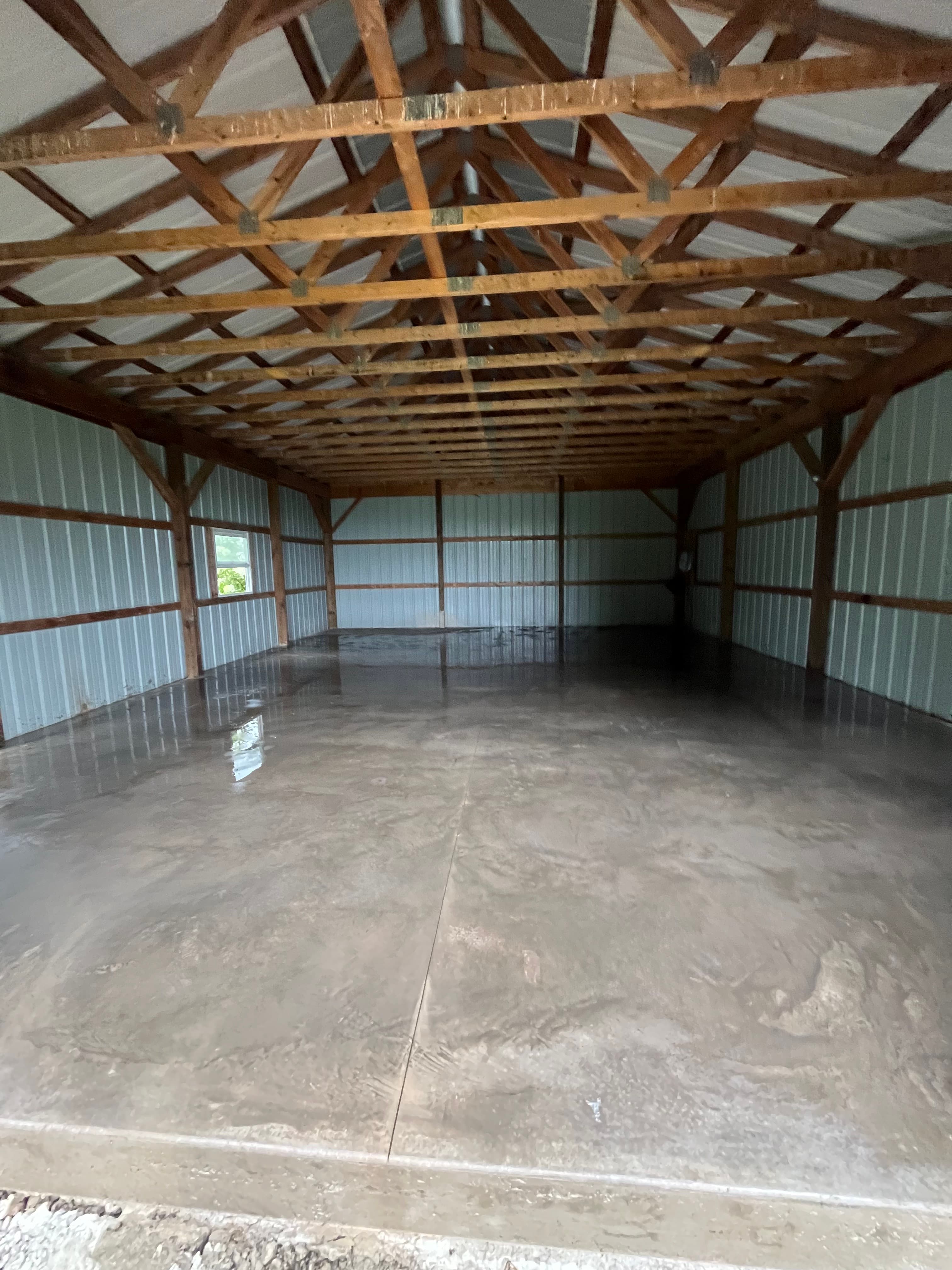 Empty barn interior with polished concrete floors and a detailed wooden truss roof structure.