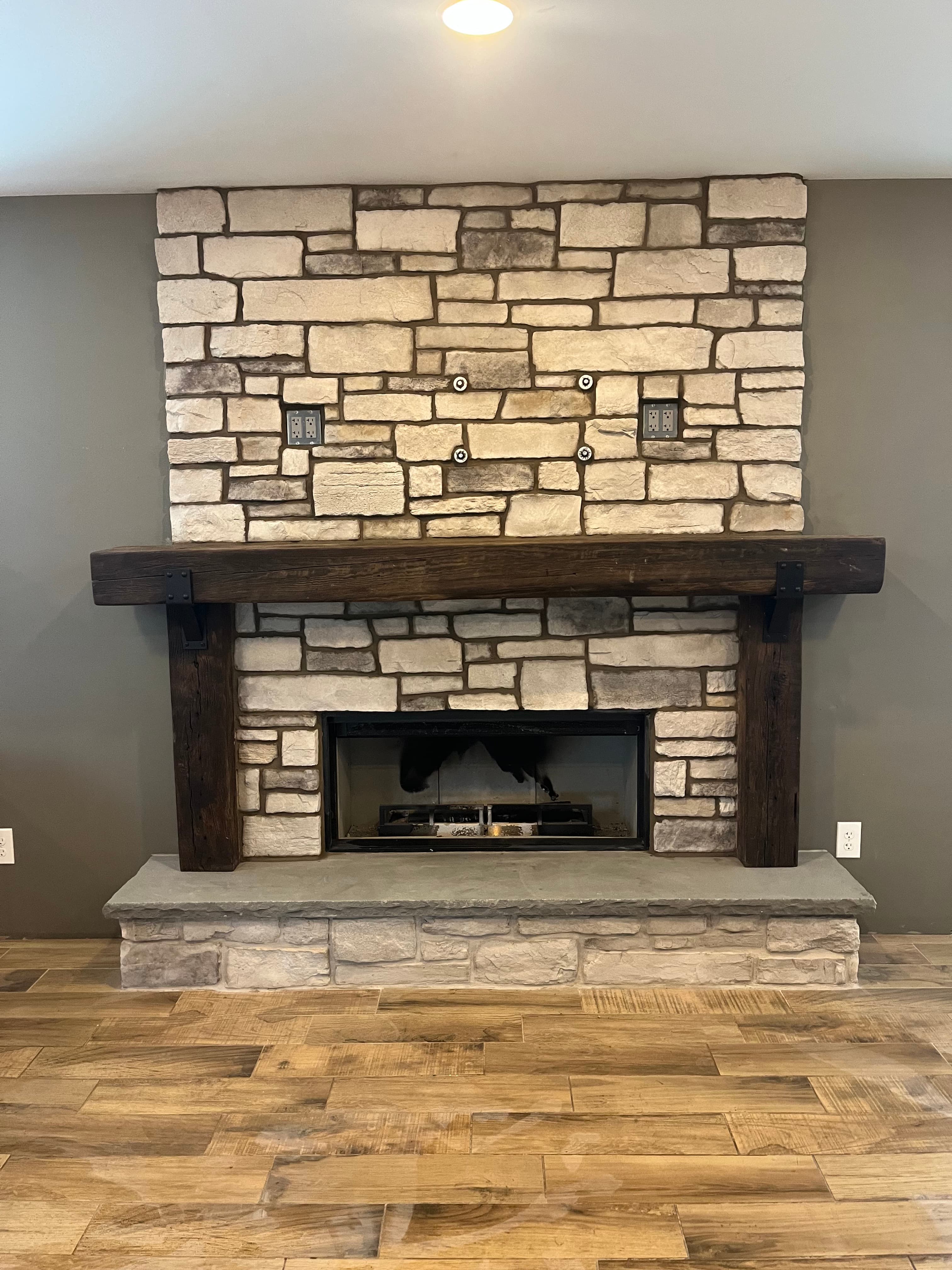 Modern rustic fireplace featuring light stacked stone, a dark wood mantel, and black fireplace insert.